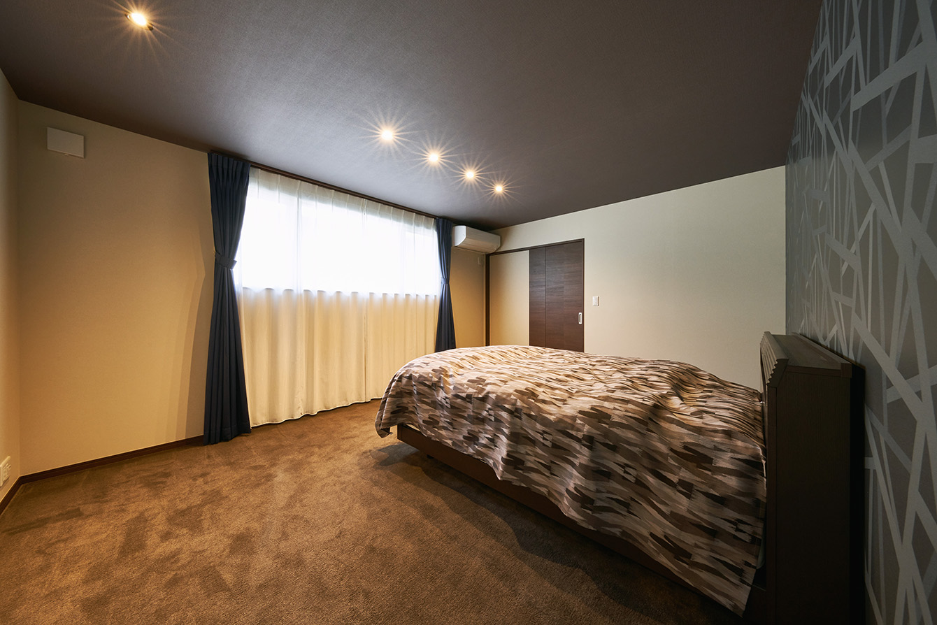 寝室は壁、天井のクロスをダークカラーにすることで落ち着いた空間に。腰高窓に長いカーテンを設置して重厚感を演出。
