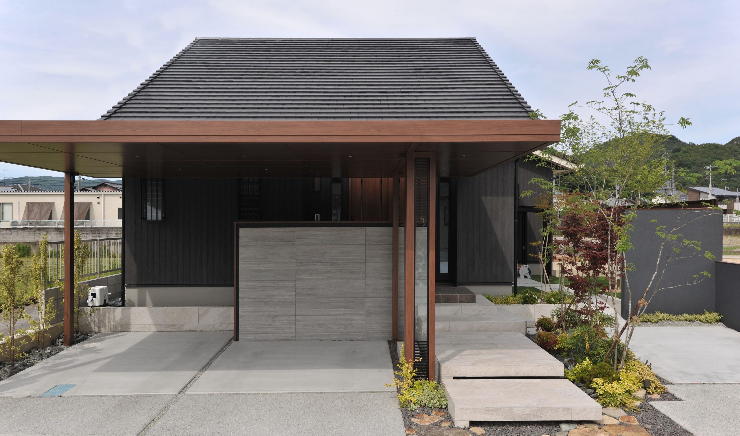 草木のシルエットを際立たせる黒を基調とした外壁に、下屋のように住まいと一体にとなったカーポート屋根が特徴。